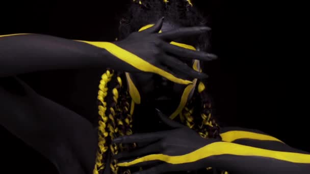 Face art. Femme dansante avec peinture pour le corps noir et jaune. Jeune fille africaine avec peinture colorée du corps. Un modèle afro-américain étonnant avec un maquillage jaune. Gros plan sur le visage. — Video
