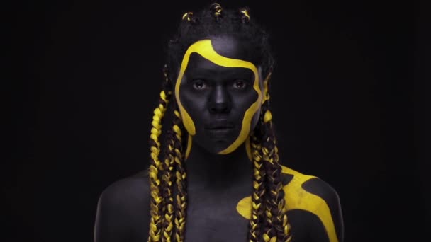 Twarzą w twarz. Krzycząca dzika kobieta z czarno-żółtą farbą do ciała. Młoda afrykańska dziewczyna z kolorowym farbą do ciała. Niesamowity afro amerykański model z żółtym makijażem. — Wideo stockowe