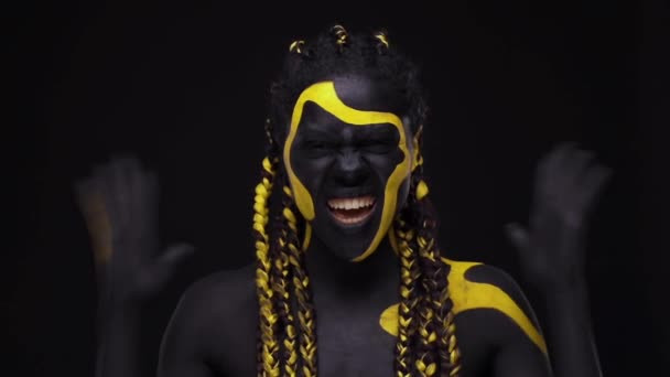 Gesichtskunst. Schreiend knurrende wilde Frau mit schwarz-gelber Körperfarbe. Junges afrikanisches Mädchen mit farbenfroher Bodypaint. Ein erstaunliches afroamerikanisches Model mit gelbem Make-up. — Stockvideo