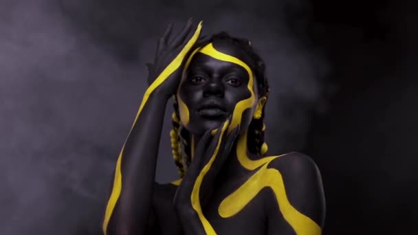 Face art. Femeia care dansează cu vopsea neagră şi galbenă. O tânără africană cu vopsea colorată. Un model afro-american uimitor cu machiaj galben. Față de închidere . — Videoclip de stoc