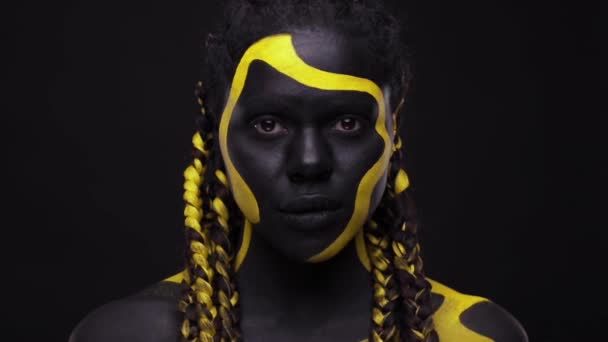 Obličej. Žena s černou a žlutou barvou na tělo. Mladá africká dívka s barevným nátěrem. Úžasný afro americký model se žlutým make-upem. — Stock video