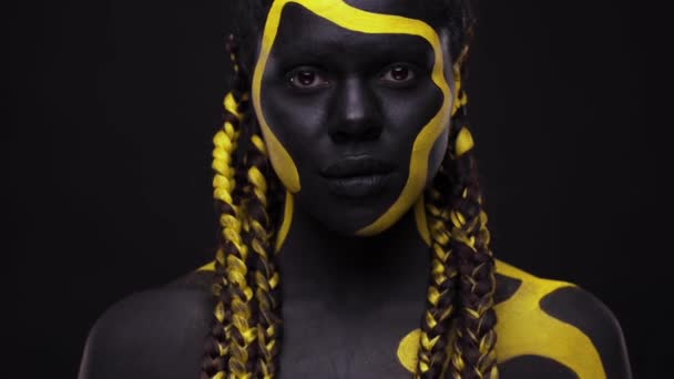Τέχνη προσώπου. Γυναίκα με μαύρο και κίτρινο χρώμα σώματος. Νεαρό κορίτσι από την Αφρική με πολύχρωμο μπογιές. Ένα καταπληκτικό afro american μοντέλο με κίτρινο μακιγιάζ. — Αρχείο Βίντεο