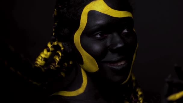 Cara de arte. Mujer bailarina con pintura corporal negra y amarilla. Chica africana joven con colorido bodypaint. Un increíble modelo afro-americano con maquillaje amarillo. Cara de primer plano. — Vídeo de stock