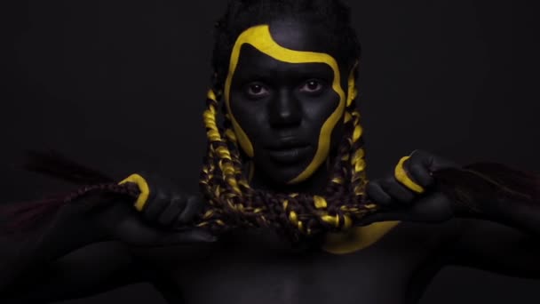 ศิลปะใบหน้า ผู้หญิงที่เต้นรําด้วยสีร่างกายสีดําและสีเหลือง เด็กสาวชาวแอฟริกันที่มีสีสันทาสีร่างกาย โมเดลแอฟโรอเมริกันที่น่าทึ่งพร้อมเครื่องสําอางสีเหลือง ปิดหน้า . — วีดีโอสต็อก