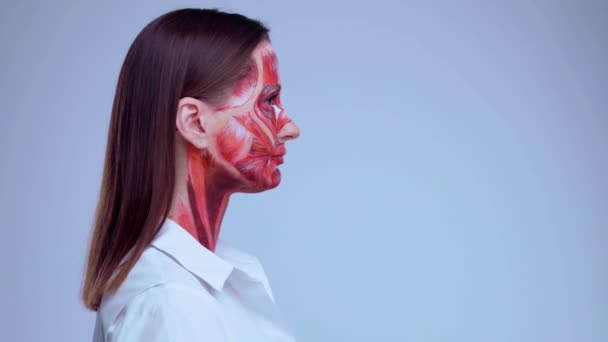 皮膚の下の筋肉構造を持つ顔の半分を持つ若い女性.軽い背景で医療訓練のためのモデル。顔のビデオを閉じます人間の解剖学. — ストック動画