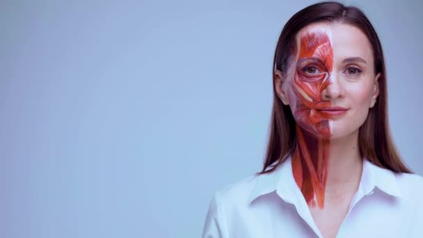 Mladá žena s polovinou obličeje s svalovou strukturou pod kůží ukazuje vlevo na kopírovací prostor.. Model pro lékařský výcvik na lehkém pozadí. Detailní video lidské antomie obličeje. — Stock video