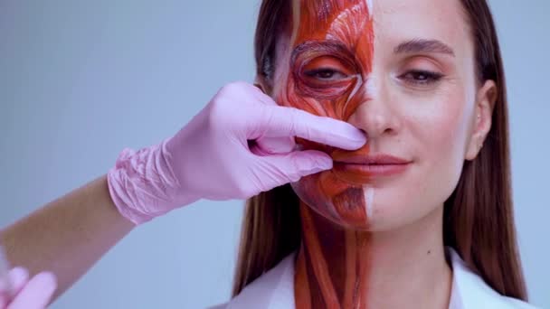 Botox injection in the face. Young woman with half of face with muscles structure under skin. Model for medical training on a light background. Close up video of face human anantomy. — Stock Video