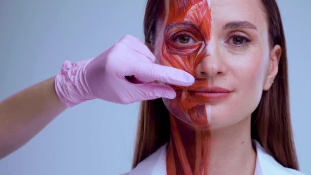 Cosmetic injection in the face. Young woman with half of face with muscles structure under skin. Model for medical training on a light background. Close up video of face human anantomy. — Stock Video