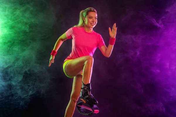 Um atlético forte, corredor feminino no bacground preto vestindo uma roupa apertada, fitness. Menina de esportes em sapatos para salto kangoo. Mulher loira e atleta fitness isolado no fundo de cor. — Fotografia de Stock