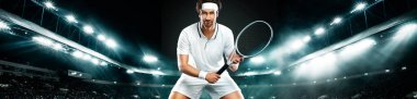 Beyaz tişörtlü tenisçi. Tenis kortlarıyla büyük arenada oynayan erkek sporcu. Geniş pankart