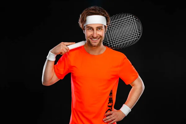 オレンジ色のTシャツにラケットを持つ笑顔のテニス選手。黒人を背景に孤立したプレーをする男選手. — ストック写真