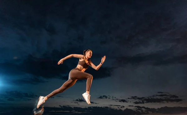 Sprinter in marcia. Forte donna atletica che corre su sfondo nero indossando lo sportswear. Fitness e motivazione sportiva. Concetto corridore. — Foto Stock