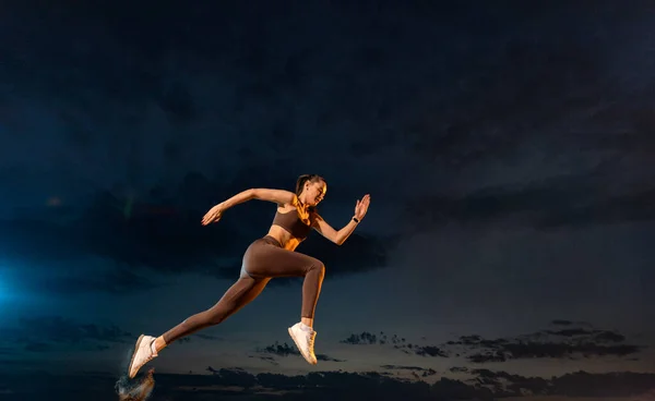 Sprinter in marcia. Forte donna atletica che corre su sfondo nero indossando lo sportswear. Fitness e motivazione sportiva. Concetto corridore. — Foto Stock