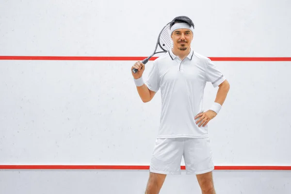 Un joueur de squash sur un terrain de squash avec la raquette. Vêtements de sport blancs. — Photo