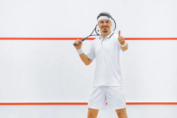 Un joueur de squash sur un terrain de squash avec la raquette. Vêtements de sport blancs. — Photo