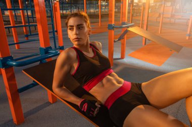Açık hava spor sahasında abdominal mekik çeken genç bir kız.