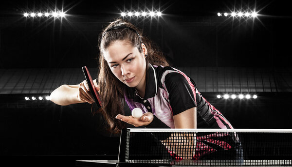Young pretty sporty girl playing table tennis on black background with lights