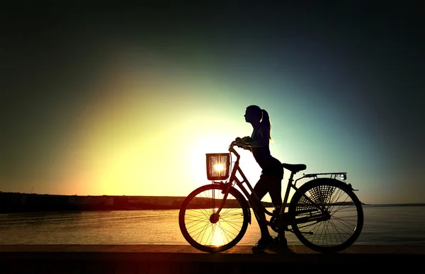 Silhouette of the beautiful streight woman with bicycle on sunset near a sea — Stock Photo, Image