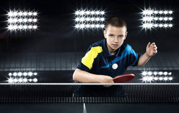 Little boy tennis-player in play on black background. Action shot.