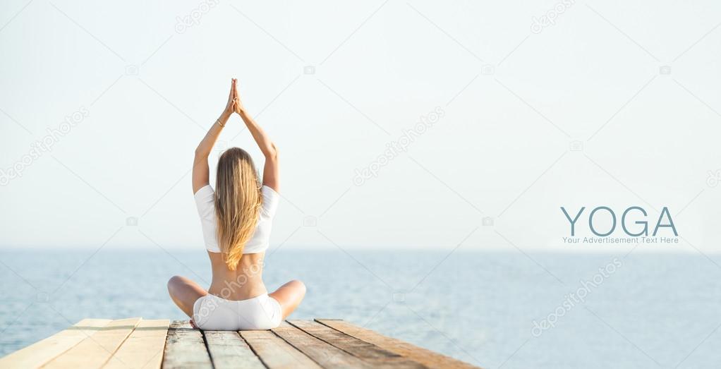 Beautiful positiveblond girl practicing yoga at seashore and meditating 