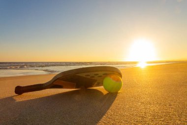 Vibrant sunset over the calm ocean with beach tennis equipment on the shore. Ideal concept for leisure, fitness, and active vacation