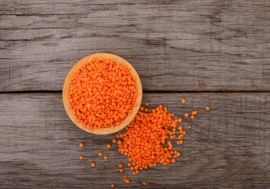 Kırsal ahşap arka planda dağınık tahıllar, sağlıklı besin maddeleri ve vejetaryen protein kaynağı olan ahşap bir kasede kırmızı mercimek.