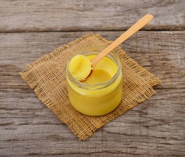 Geleneksel yağ yağının otantik fotoğrafçılığı. Bu gerçek kamera görüntüsü bir kavanoz sarı berrak tereyağını gösteriyor. Çuval bezi ve ahşap masa üzerinde kaşık var. Sağlıklı organik yağları vurguluyor..