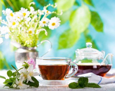 Güneşli bir günde bir fincan çay ve çiçek.