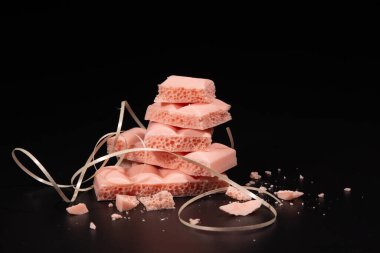 Siyah arka planda havalanmış pembe çikolata parçaları.