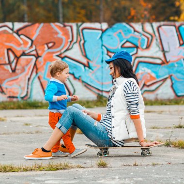 anne oğluna kaykay sürmeyi öğretiyor.