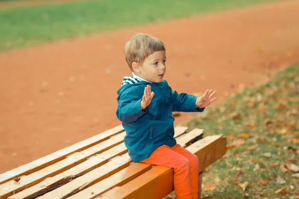 Malý chlapec sedí na lavičce v parku — Stock fotografie