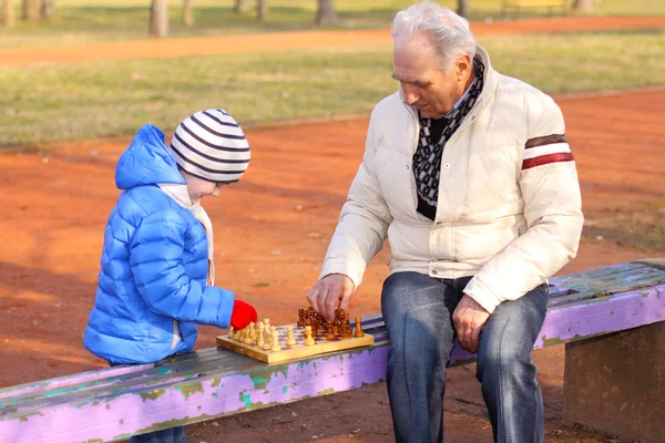 Дедушка и внук играют в шахматы на открытом воздухе — стоковое фото