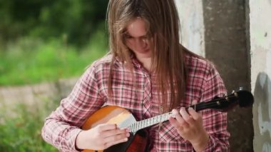 Uzun saçlı güzel duygusal bir kız beton bir duvarın arkasında müzik aleti çalıyor. Şiddetli rüzgar saçı savurur. Genç ve çekici bir kız müzik aleti çalmaktan hoşlanıyor. Domra. Halk enstrümanı. Duvara yaslan.. 