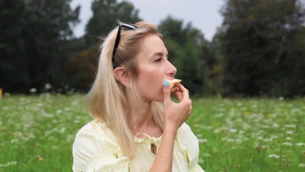 Een mooi meisje eet een taart en drinkt koffie in het park. — Stockvideo