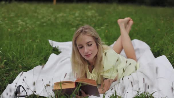 Красива дівчина читає книгу в парку — стокове відео
