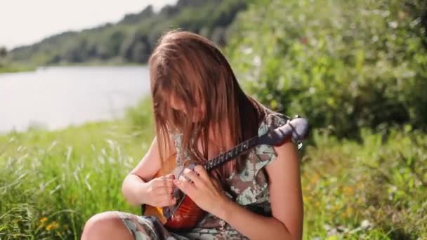 Junge schöne Mädchen spielt ein Musikinstrument auf dem Hintergrund des Flusses. — Stockvideo