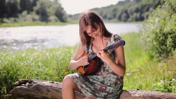 Young beautiful girl plays a musical instrument on the background of the river. — Stock Video
