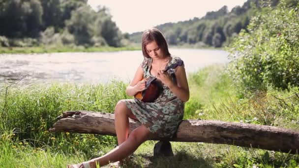 Young beautiful girl plays a musical instrument on the background of the river — Stock Video
