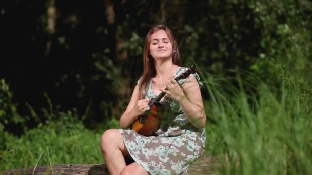 Jovem menina bonita toca um instrumento musical no fundo do rio — Vídeo de Stock