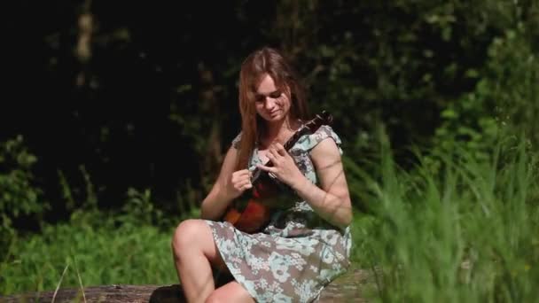 Ung vacker flicka spelar ett musikinstrument på bakgrunden av floden — Stockvideo