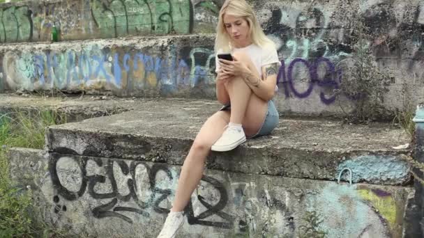 Een Mooie Blonde Kijkt Haar Mobieltje Een Hippe Meid Leest — Stockvideo