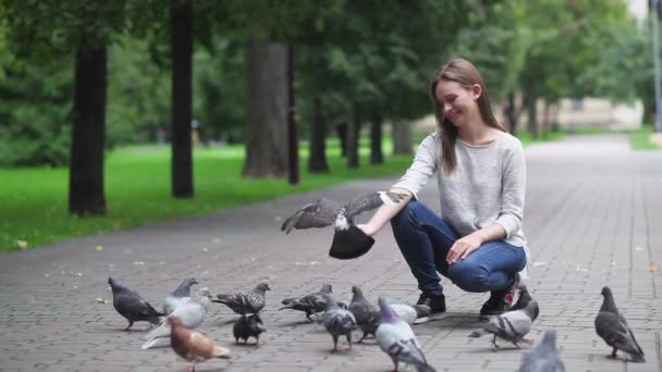 Atraktivní šťastná dívka, která krmí holuby v parku. Zpomalený pohyb — Stock video