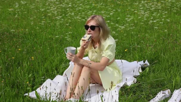 Beautiful young woman eating a cake and drinking coffee in the park — Stock Video