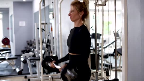 Una hermosa chica deportiva se dedica al gimnasio. Levantando brazos con una barra mientras está de pie — Vídeo de stock