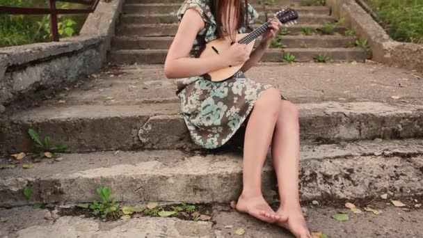 Junge schöne Mädchen spielen ein Musikinstrument Mandoline, während sie auf der Treppe sitzen — Stockvideo