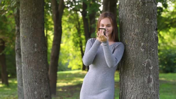 Schöne Mädchen mit langen Haaren glättet Make-up im Park — Stockvideo