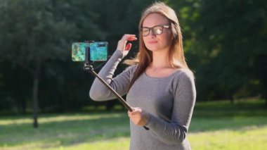 Uzun saçlı güzel kız dışarıda parkta selfie çekiyor.