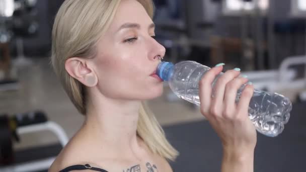 아름다운 금발의 여자 가 체육관에 갑니다. 훈련받는 동안 물을 마시는 소녀. — 비디오