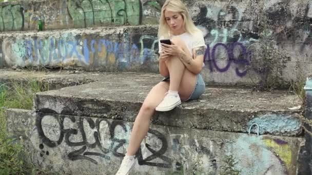 Hermosa rubia mira en su teléfono celular — Vídeos de Stock