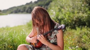 Genç ve güzel bir kız nehrin arka planında bir müzik aleti çalıyor.